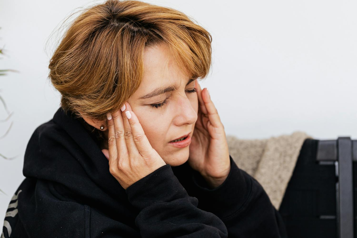 A woman wincing in pain and holding the sides of her head, experiencing ear pain