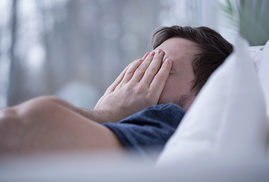 A man lying in bed covering his face, unable to fall asleep